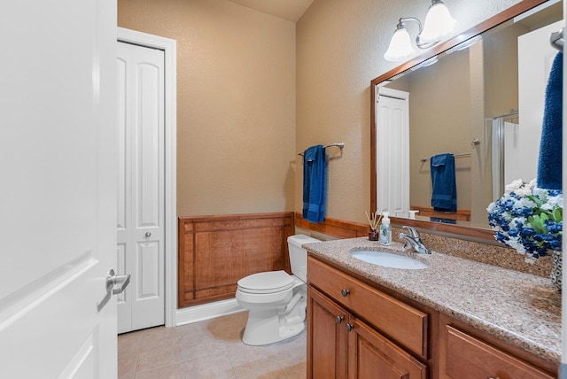 full bathroom with a shower with door, a wainscoted wall, toilet, tile patterned floors, and vanity