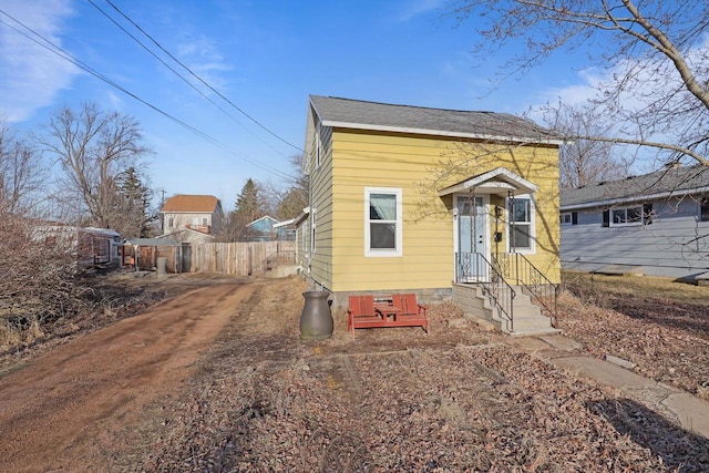 view of front of house featuring fence, dirt driveway, and roof with shingles