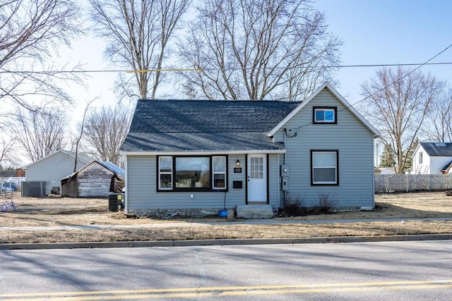 view of front of house with cooling unit, fence, and roof with shingles