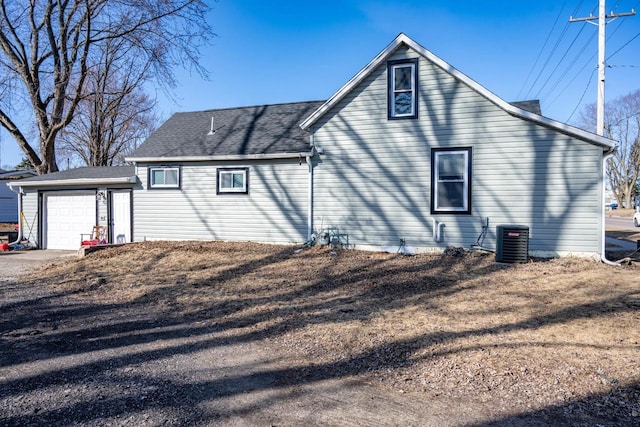 rear view of house with cooling unit, roof with shingles, concrete driveway, and an attached garage