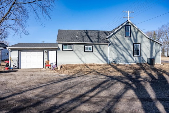 rear view of property featuring an attached garage, cooling unit, driveway, and a shingled roof