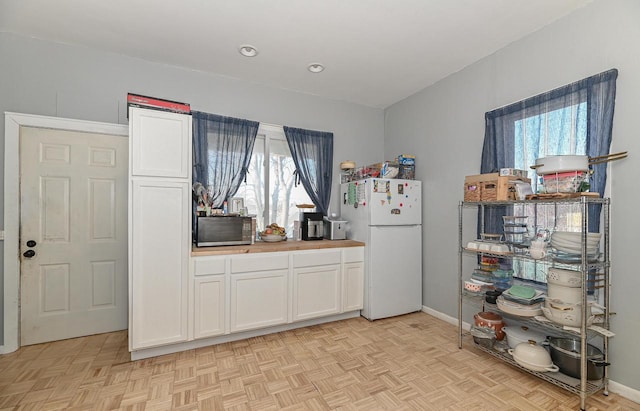 kitchen featuring baseboards, white cabinetry, wooden counters, and freestanding refrigerator