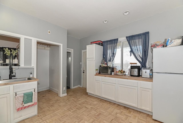 kitchen with white cabinetry, baseboards, freestanding refrigerator, and a sink