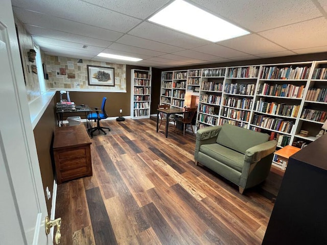 office area with wall of books, wood finished floors, baseboards, and a paneled ceiling