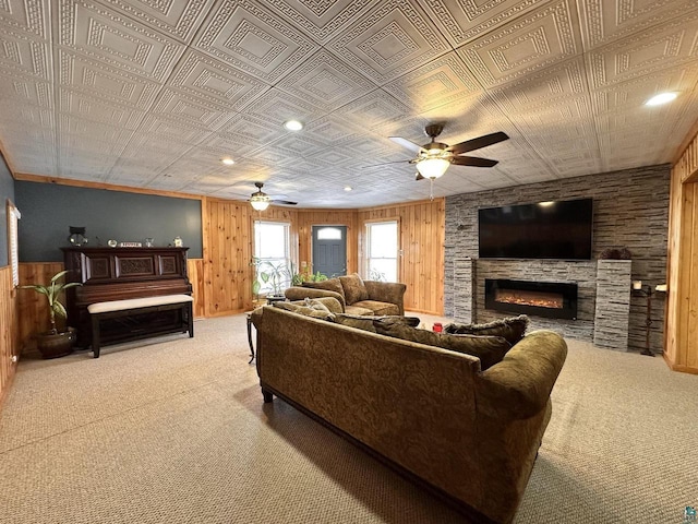 carpeted living room featuring a ceiling fan, a fireplace, wood walls, and an ornate ceiling