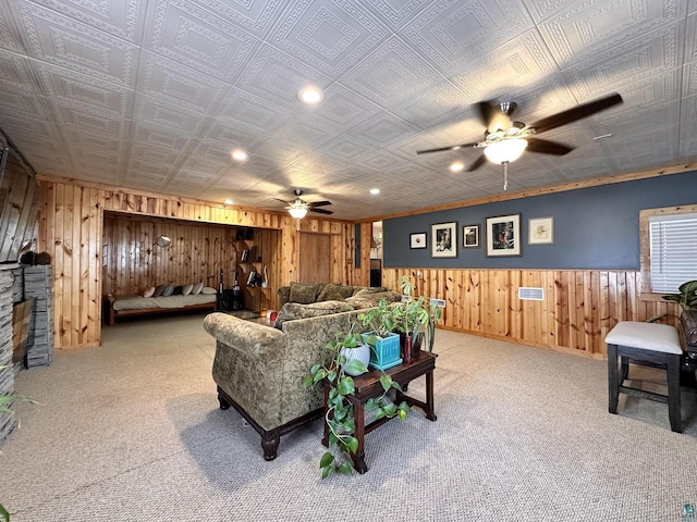 living area with carpet flooring, visible vents, a ceiling fan, and wooden walls