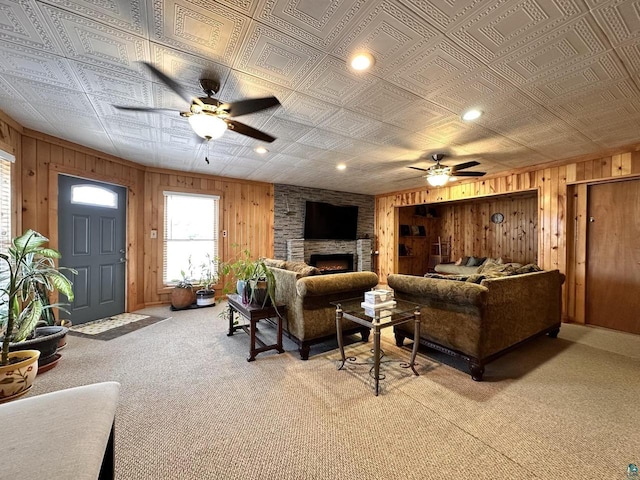 living area featuring a stone fireplace, wooden walls, light colored carpet, and an ornate ceiling