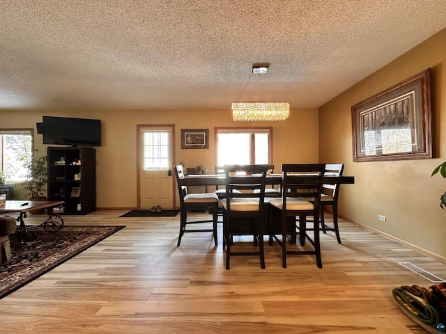 dining room featuring light wood-type flooring, baseboards, and a textured ceiling