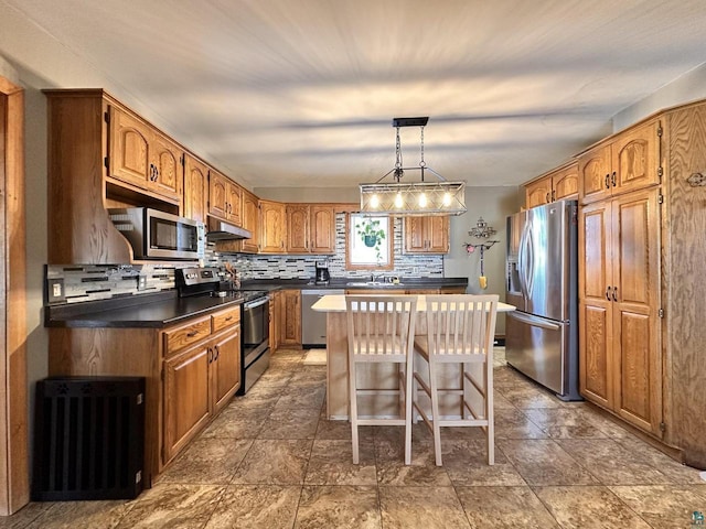 kitchen featuring brown cabinetry, decorative backsplash, under cabinet range hood, appliances with stainless steel finishes, and a center island