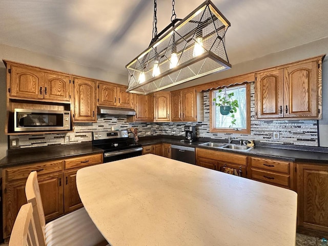 kitchen with tasteful backsplash, under cabinet range hood, appliances with stainless steel finishes, brown cabinetry, and a sink