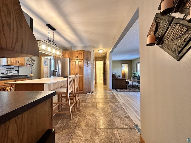 kitchen with dark countertops, visible vents, backsplash, pendant lighting, and stainless steel refrigerator with ice dispenser