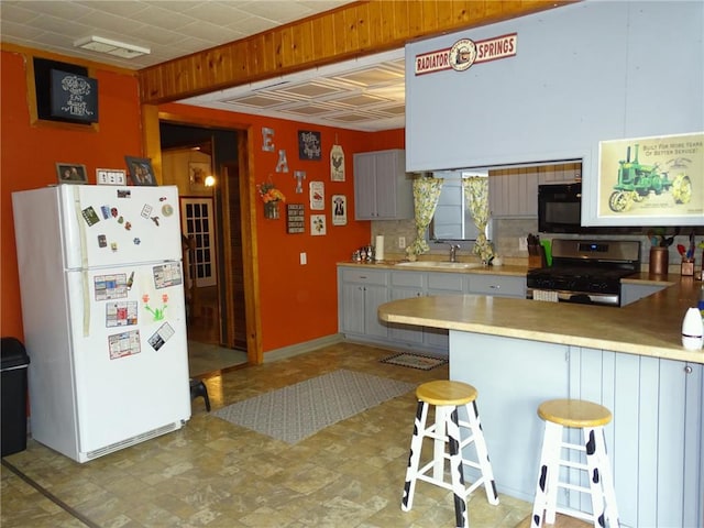 kitchen with a kitchen bar, a peninsula, freestanding refrigerator, stainless steel gas stove, and a sink