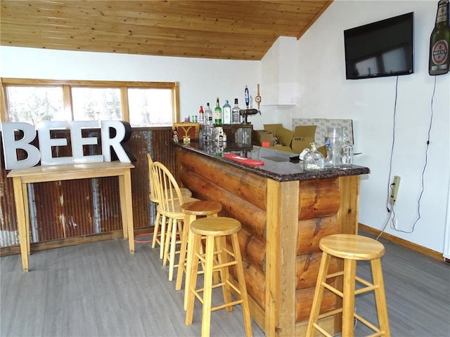 bar featuring wood finished floors, a bar, baseboards, wood ceiling, and vaulted ceiling