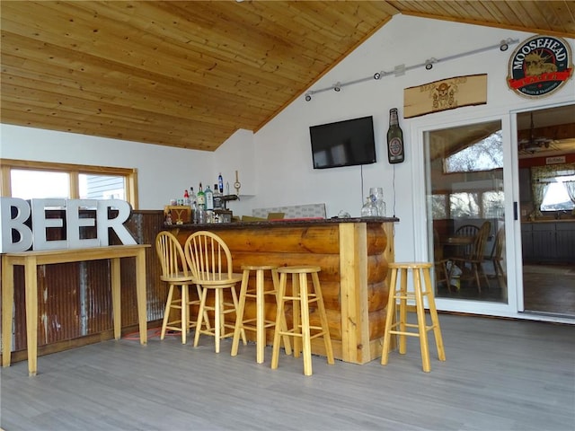 bar with wood ceiling, wood finished floors, a bar, and vaulted ceiling