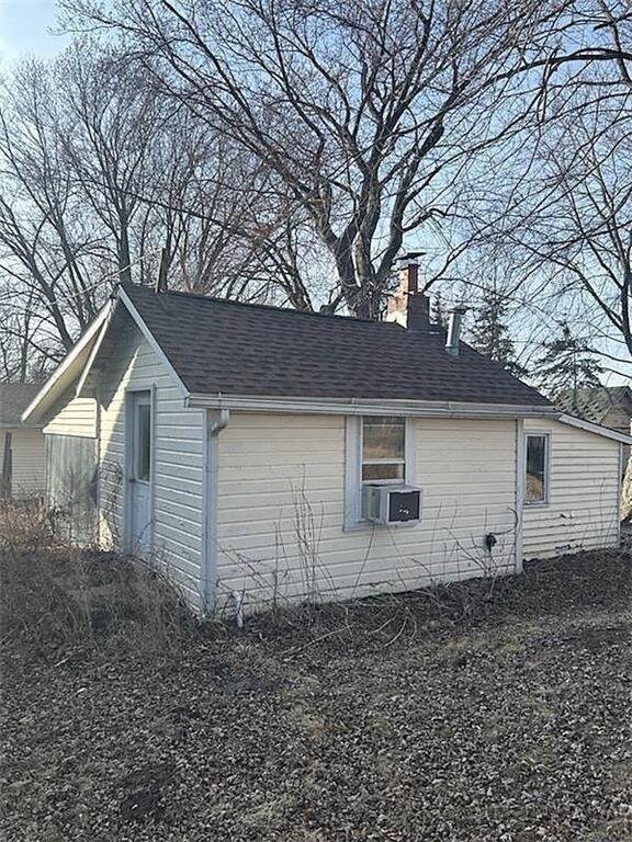 view of side of home with cooling unit, a chimney, and a shingled roof