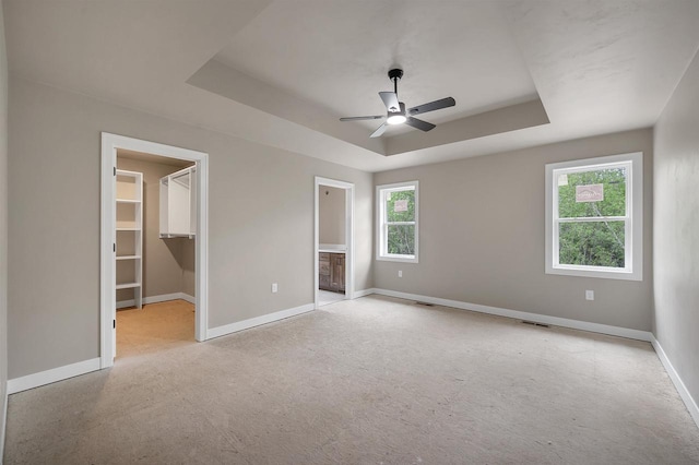 2570 Meyer Way, De Pere, WI 54115 - unfurnished bedroom with baseboards, a tray ceiling, a walk in closet, ensuite bathroom, and a ceiling fan