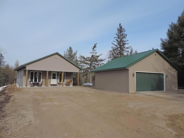 ranch-style house with covered porch, metal roof, a detached garage, and an outdoor structure