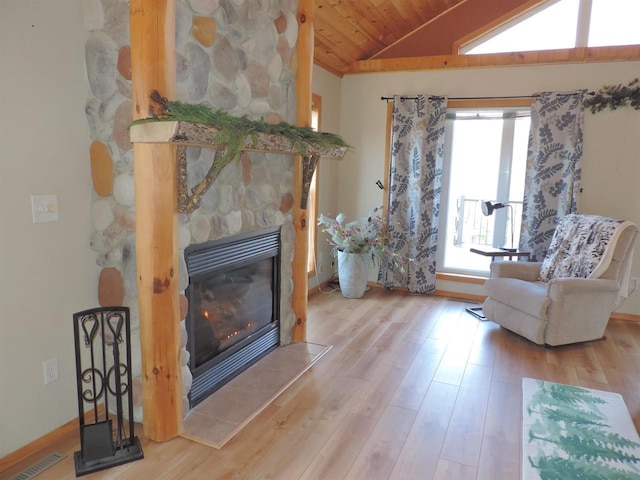 living area with visible vents, wood ceiling, vaulted ceiling, a stone fireplace, and wood finished floors