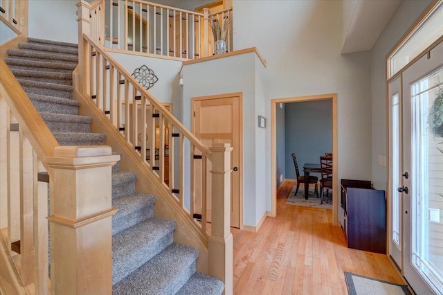 foyer entrance featuring stairs, a high ceiling, baseboards, and light wood finished floors