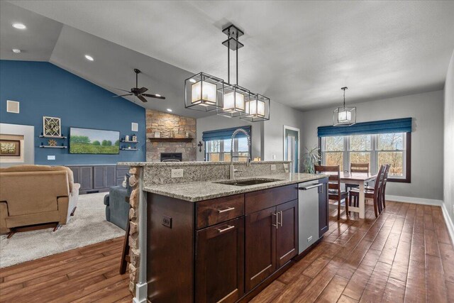 kitchen with dark wood-type flooring, a sink, open floor plan, dark brown cabinetry, and a stone fireplace