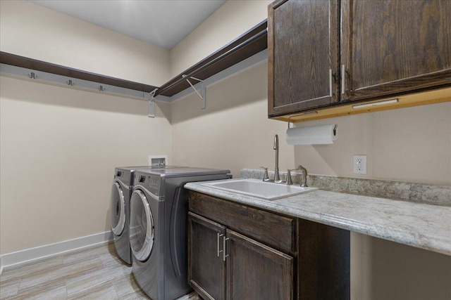 washroom with baseboards, separate washer and dryer, cabinet space, a sink, and light wood-type flooring