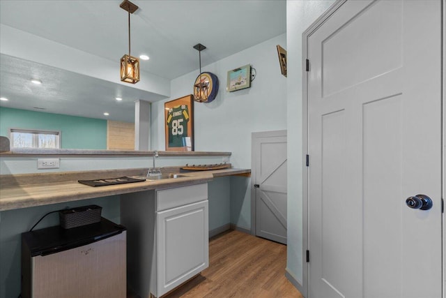 kitchen with light wood-style flooring, decorative light fixtures, a sink, white cabinetry, and light countertops