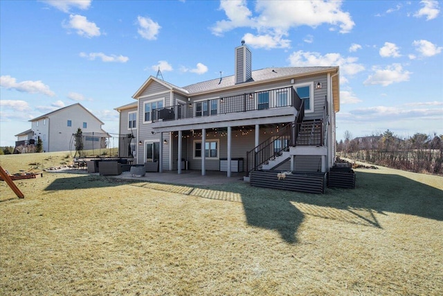 back of house featuring a lawn, a patio, stairs, a wooden deck, and a chimney