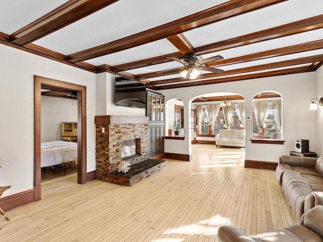 living area with arched walkways, a fireplace, baseboards, and light wood-style floors