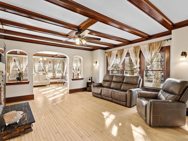 living area featuring a ceiling fan, baseboards, arched walkways, wood-type flooring, and beamed ceiling