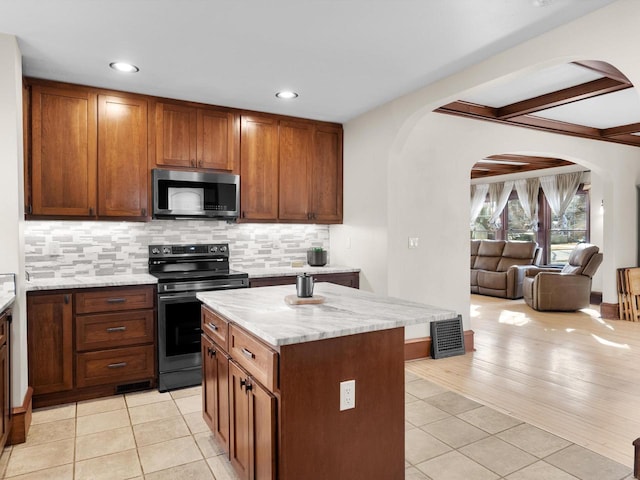 kitchen featuring light tile patterned floors, backsplash, appliances with stainless steel finishes, and arched walkways