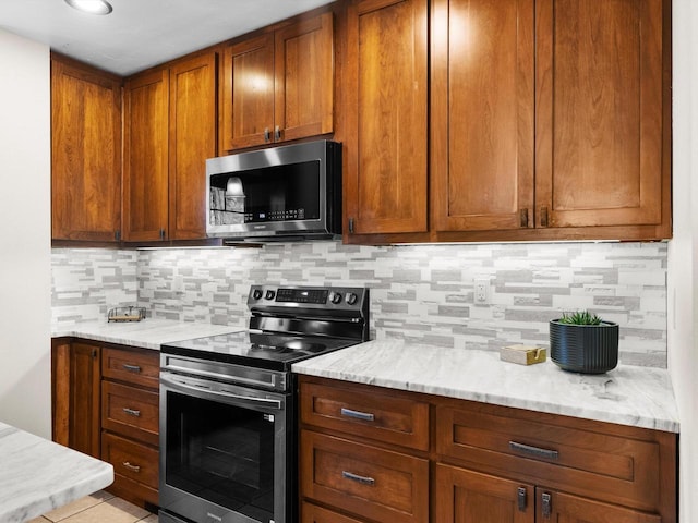 kitchen with light stone countertops, brown cabinetry, backsplash, and stainless steel appliances