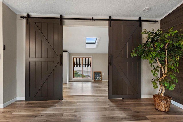 foyer entrance with a barn door, baseboards, a textured ceiling, and light wood-style flooring