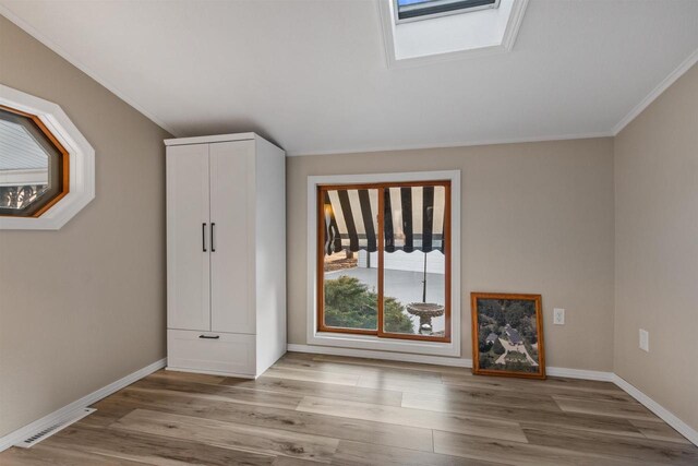 unfurnished bedroom featuring visible vents, wood finished floors, a skylight, crown molding, and baseboards