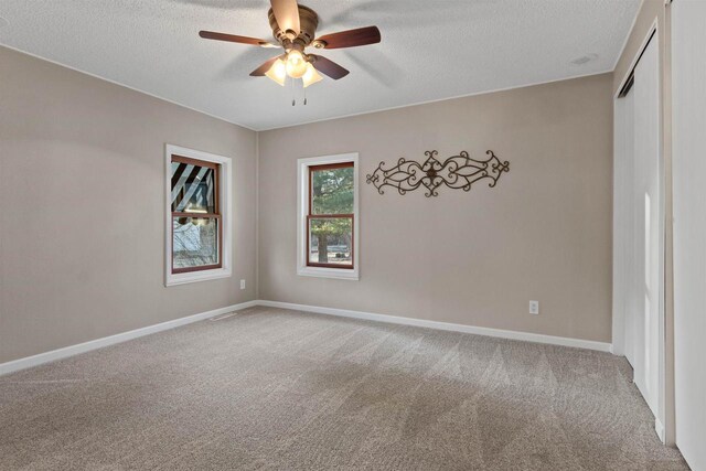 carpeted spare room featuring ceiling fan, a textured ceiling, and baseboards