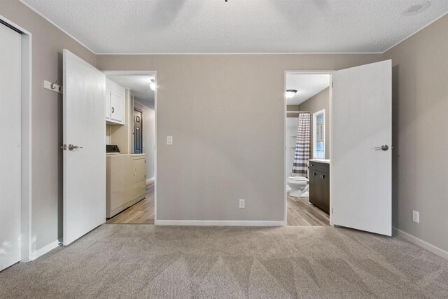 unfurnished bedroom with light carpet, washer / clothes dryer, a textured ceiling, ensuite bath, and baseboards