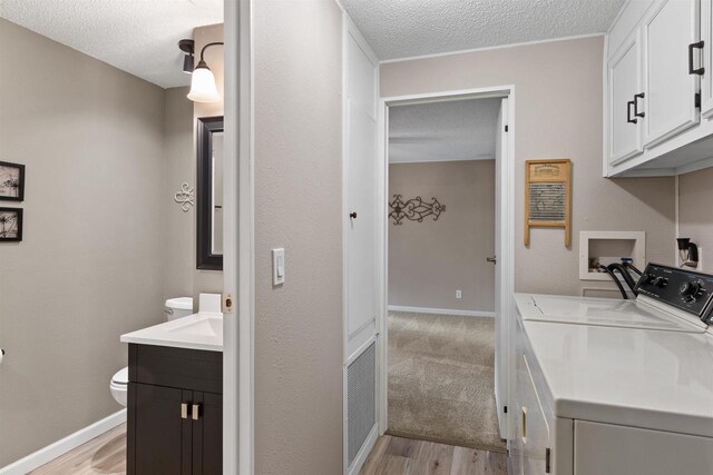 laundry area featuring light wood-type flooring, baseboards, a textured ceiling, and washing machine and clothes dryer