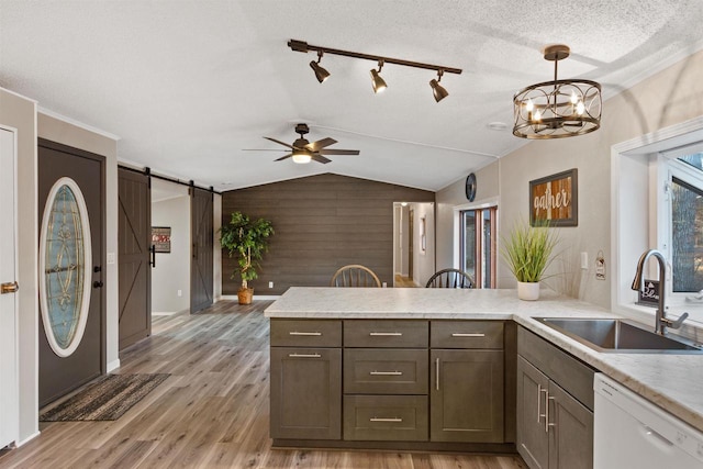 kitchen featuring lofted ceiling, white dishwasher, a sink, light wood-style floors, and a barn door