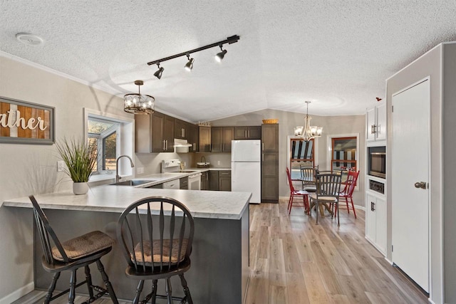 kitchen with light wood finished floors, a notable chandelier, a sink, white appliances, and light countertops