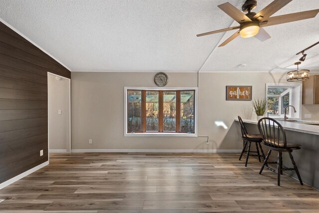 dining area with lofted ceiling, a textured ceiling, wood finished floors, wooden walls, and baseboards