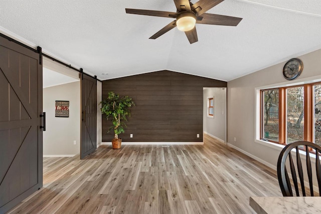 interior space with wooden walls, light wood-style flooring, a barn door, and vaulted ceiling