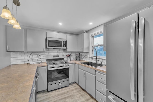 kitchen featuring gray cabinets, a sink, stainless steel appliances, light countertops, and tasteful backsplash