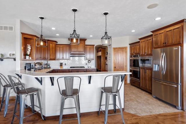 kitchen with visible vents, under cabinet range hood, brown cabinets, a peninsula, and stainless steel appliances