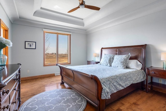 bedroom with baseboards, a raised ceiling, wood finished floors, and a ceiling fan