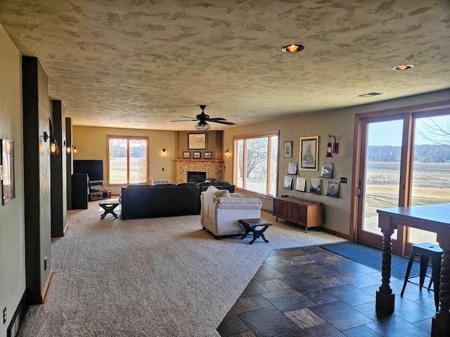 living room featuring visible vents, baseboards, stone tile floors, a fireplace, and a ceiling fan