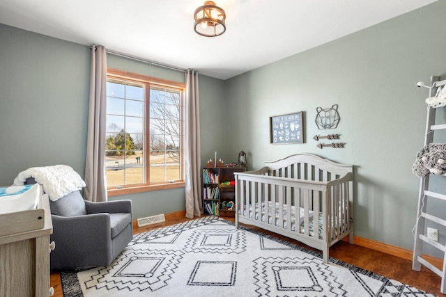 bedroom featuring wood finished floors, a nursery area, visible vents, and baseboards