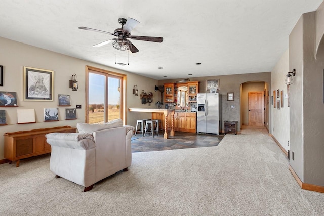 carpeted living area with baseboards, arched walkways, and a ceiling fan