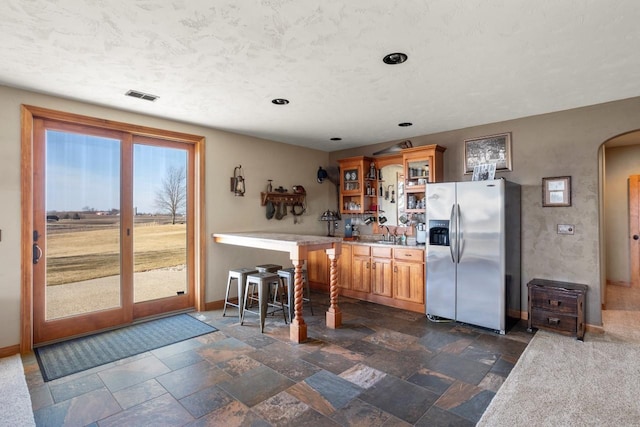 kitchen with visible vents, arched walkways, light countertops, glass insert cabinets, and stainless steel fridge