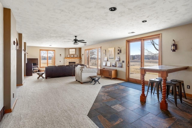 living room featuring a fireplace, a ceiling fan, baseboards, and a textured ceiling