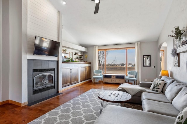 living room with lofted ceiling, wood finished floors, arched walkways, baseboards, and a tile fireplace