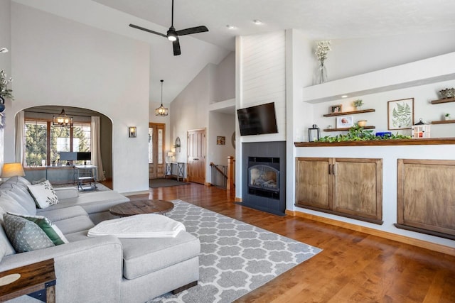 living area with high vaulted ceiling, a ceiling fan, wood finished floors, a large fireplace, and arched walkways